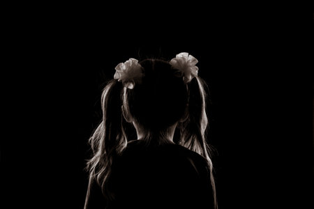 silhouette of a girl with two ponytails sitting with her back in the dark. anonymity and child safety conceptの写真素材