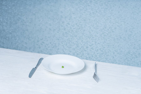 a table with a plate in which there is only one pea. concept of diet for weight loss. eating disorder.の写真素材