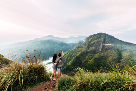 A couple in love is photographed on the phone. Boy and girl in the mountains. Man and woman holding hands. The couple travels around Asia. Travel to Sri Lanka. Serpentine in the mountains. Loverの写真素材