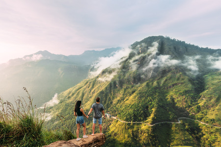 The couple greets the sunrise in the mountains. Boy and girl in the mountains. Man and woman holding hands. The couple travels around Asia. Travel to Sri Lanka. Serpentine in the mountains. Honeymoonの写真素材