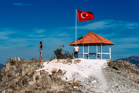 Boy and girl standing on a rock. A couple in love travels. A couple in Turkey. Man and woman. A guy and a girl. Honeymoon trip. Couple on nature. Boy and girl by the flagの写真素材