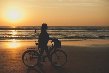 A woman makes an evening bike ride along the sea. People walk along the sea at sunset. Sunset on sea. Silhouette of people. Travelers at sunset. Tourists on vacationの写真素材
