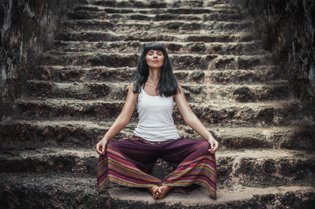 Girl in Lotus position. Attractive girl doing yoga. Healthy lifestyle. A person meditates in the temple. The concentration of the body. Holidays in Asia. Stairs of the old temple. Buddhist templeの写真素材