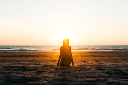 Silhouette of a girl on the beach at sunset. Girl doing yoga on the beach. Silhouette of a woman on the beach. Sea tour. Lonely girl at sunset. Warm, bright, evening sun. Asian holidays in GOAの写真素材