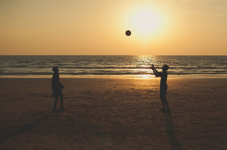 Children play ball on the sea. Beach volleyball. Silhouette of people who play ball in the evening....