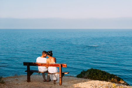 Couple in love at sunset. Man and woman at dawn. Couple sitting on a bench by the sea. Couple kissing by the sea. Honeymoon trip. Sunset on sea. Dawn by the sea. Wedding travel. Sunrise on the shoreの写真素材