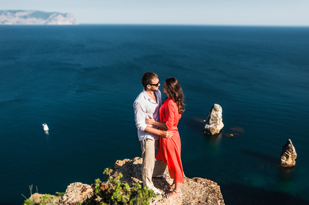 Couple in love at sunset by the sea. Honeymoon. Honeymoon trip. Boy and girl at the sea. Man and woman traveling. Couple hugs. Couple kissing. Newly married couple. Lovers. Holiday romanceの写真素材