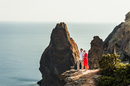 Couple in love at sunset by the sea. Honeymoon. Honeymoon trip. Boy and girl at the sea. Man and woman traveling. Couple hugs. Couple kissing. Newly married couple. Lovers. Holiday romanceの写真素材