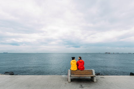 Young couple sitting on a bench by the sea. Man and woman traveling. People sit on a bench and look...