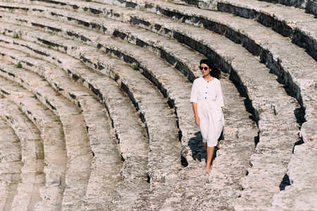 Girl walking on the steps of an ancient amphitheater, located in Hierapolis, Pamukkale, Denizli province, Turkey. Beautiful girl on the steps. Girl in white dress on stone stairsの写真素材