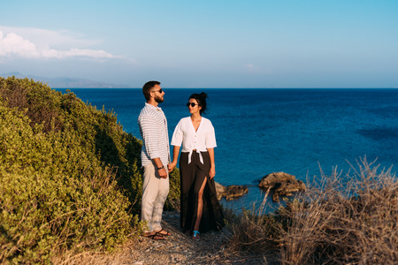 Couple in love at sunset by the sea. Honeymoon. Honeymoon trip. Boy and girl at the sea. Man and woman traveling. Couple hugs. Couple kissing. Newly married couple. Lovers. Holiday romanceの写真素材