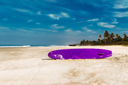 Surfboard on a tropical beach overlooking the ocean, blue sky background. Colored Board for surfing on the sand.の写真素材