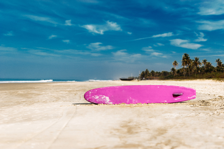 Surfboard on a tropical beach overlooking the ocean, blue sky background. Colored Board for surfing on the sand.の写真素材