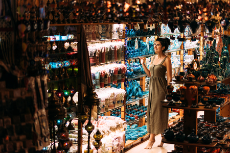 Beautiful girl in a souvenir shop in Turkey. Girl chooses a souvenir Oriental shop. Street shop. Turkish Souvenirs. Oriental bazaar. Turkish Bazaar. Tourist shop. Moroccan Bazaar.の写真素材
