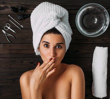 Portrait of young beautiful woman in spa environment. A woman takes care of her body. Female body care. Nail care manicure and pedicure. Girl with a towel on her head. The girl looks at the cameraの写真素材