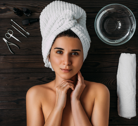 Portrait of young beautiful woman in spa environment. A woman takes care of her body. Female body care. Nail care manicure and pedicure. Girl with a towel on her head. The girl looks at the cameraの写真素材
