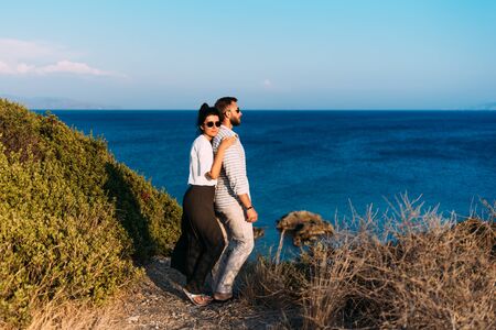 Couple in love at sunset by the sea. Happy couple at sunset.Honeymoon. Honeymoon trip. Boy and girl by the sea. Man and woman traveling. Newly married couple. Holiday romanceの写真素材