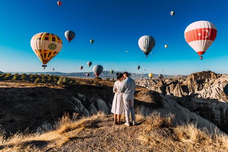 Couple travels the world. Honeymoon trip. Married couple on vacation. Tourists in Cappadocia. Man and woman resting in Turkey. Flying balloons at sunrise. World tour. Man and woman among balloonsの写真素材