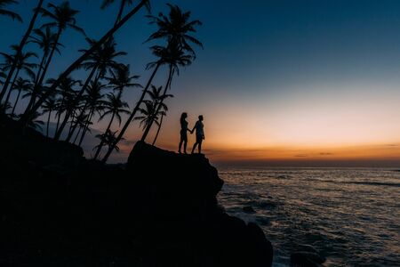 Silhouette of loving couple on sea. Man and woman at sunset. Honeymoon on the Islands. Man and woman meet sunset. Happy loving couple. Silhouette lovers. Wedding travel. Loving couple. Honeymoon tripの写真素材