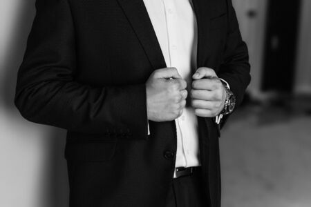 Man in business suit. A man puts on a suit. Close-up business stylish man buttoning his jacket. A businessman in an expensive suit. Black and white photoの写真素材
