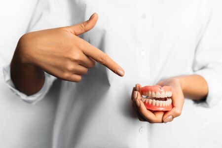 Denture in the hands of the dentist. The doctor is holding a denture. Dentistry is a Conceptual photo. Prosthetic dentistry. False teeth in the hands of a doctor. Denture close-up.の写真素材