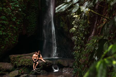 A couple in love on a waterfall. Honeymoon trip. Happy couple on the island of Bali. Beautiful couple travels the world. Travel to Indonesia. Happy couple on vacation.  Wedding tripの写真素材