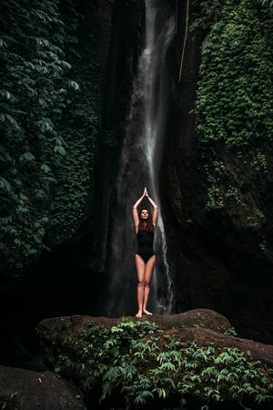 A woman does yoga at a waterfall. Healthy lifestyle. The concentration of the body. A woman does...