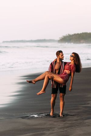 The couple is having fun on the beach. A couple in love at sunset walking along the beach. The man lifted the girl into his arms. Beautiful couple on the beach. Happy couple on vacation in Baliの写真素材