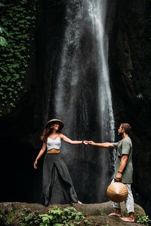 A couple in love on a waterfall. Honeymoon trip. Happy couple on the island of Bali. Beautiful couple travels the world. Travel to Indonesia. Happy couple on vacation.  Wedding trip. Copy spaceの写真素材