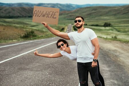 A couple hitchhiking. A man and a woman catch a car by the road. A young couple votes on the road. A man and a woman are hitchhiking. A couple hitch a ride on the road. Hitching a rideの写真素材