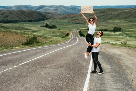 A couple hitchhiking. A man and a woman catch a car by the road. A young couple votes on the road. A man and a woman are hitchhiking. A couple hitch a ride on the road. Hitching a ride. Copy spaceの写真素材
