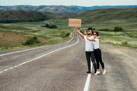 A man and a woman are hitchhiking. A young couple goes hitchhiking around the country. Free hitchhiking trip. A lover who travels free by hitchhiking. The couple goes traveling. Copy spaceの写真素材