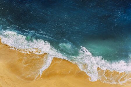Sea coast, view from the height. Yellow sandy beach with blue sea. A deserted beach with a bird's-eye view. Sea waves roll on the sandy beach. Beautiful sea landscape. Ocean, waves, sand. Copy spaceの写真素材