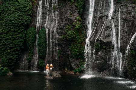 Lovers at the waterfall, rear view. Couple admiring a beautiful waterfall in Indonesia. Couple on...
