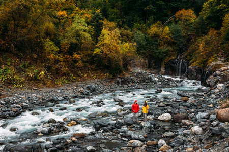 Active rest on the nature. A couple of tourists walking along a mountain river in autumn. An active couple is engaged in Hiking. A young couple is engaged in tracking. Copy spaceの写真素材