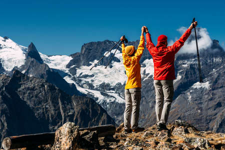 Young couple doing Nordic walking in the mountains, rear view. An active couple is engaged in Hiking. A young couple is engaged in tracking. Trekking and Nordic walking. Hiking. Copy spaceの写真素材