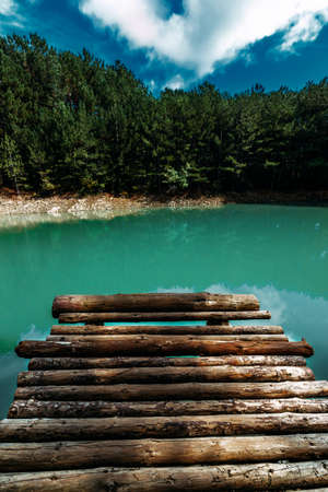 Forest lake with wooden pier, vertical view. Beautiful turquoise lake with a wooden pier in a coniferous forest. Emerald forest lake. Screen saver for your smartphone. Landscape photo on your phoneの写真素材