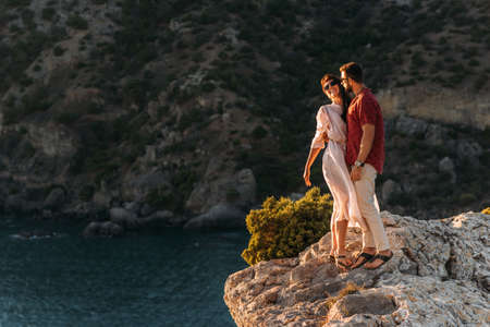 A man embraces a beautiful woman on the edge of a cliff by the sea. A couple in love at sunset. Beautiful couple meets sunset by the sea. Happy couple having fun on the coast. Copy spaceの写真素材