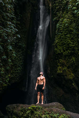 A man of athletic build at the waterfall. A man travels the world. Man at the waterfall. Travel to Bali Indonesia. A person travels through picturesque places. Lone traveler. Copy spaceの写真素材