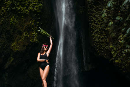Portrait of a beautiful smiling girl at the Waterfall. Portrait of a woman with a green leaf at the waterfall. Beautiful woman on the background of nature in Indonesia on the island of Bali.の写真素材