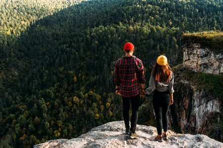 The couple greets the sunrise in the mountains, rear view. A man and a woman in the mountains. A man and a woman hold hands. A couple in love on a rock admires the beautiful views. Copy spaceの写真素材