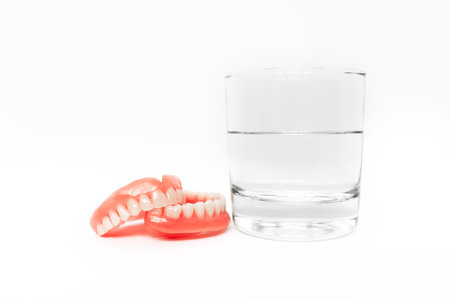 A denture in a glass of water. Dental prosthesis care. Full removable plastic denture of the jaws....