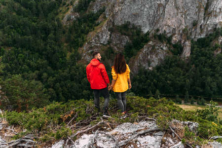 A couple in love on a rock admires the beautiful views, rear view. A man and a woman on a rock. A couple in love travels. A walk in the mountains. Couple traveling through the mountains. Hikingの写真素材