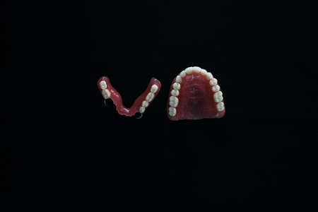 Full removable plastic denture of the jaws. A set of dentures on a black background. Two acrylic dentures. Upper and lower jaws with fake teeth. Dentures or false teeth, close-up. Copy spaceの写真素材