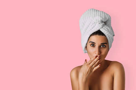 Beautiful woman with a towel on her head on a pink background. A young woman with beautiful eyes poses with a towel on her head on an isolated pink background. Bath and care concept. Spa. Copy spaceの写真素材