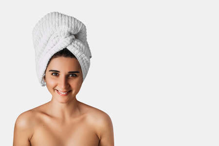 Portrait with copy space of charming pretty woman with beaming white smile after bath having towel on her head isolated on white background. Cosmetology, beauty and spa. Banner. Copy spaceの写真素材