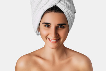 Portrait of young pretty girl smiling with towel on her head. Woman with towel on her head, close-up. Young smiling beautiful woman posing with towel on her head on white background. Spa. Skincareの写真素材
