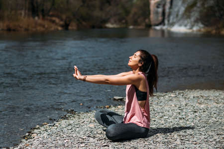 An attractive woman does yoga. Healthy lifestyle. Body concentration. A woman does yoga by the lake. A girl does yoga at dawn. A woman meditates in nature. Mountain Lake Meditation. Copy spaceの写真素材