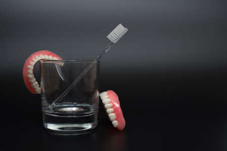 Full removable plastic denture of the jaws. Two acrylic dentures. Dental care with an toothbrush. Teeth and toothbrush on a dark background. Dental prosthesis care. Oral hygiene. Copy space.の写真素材