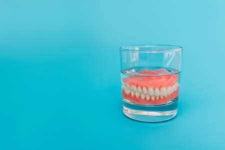 Prosthesis in a glass with a solution. Dental prosthesis care. Full removable plastic denture of the jaws. Two acrylic dentures. Upper and lower jaws with fake teeth. Dentures or false teeth, close-upの写真素材